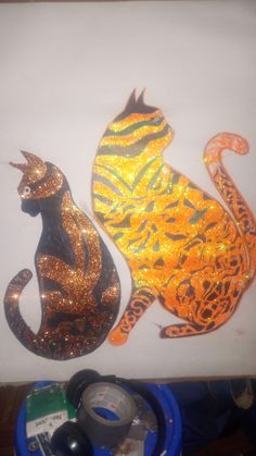 two glass cats sitting next to each other on top of a white board covered in glitter