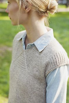 a woman standing in the grass with her hair pulled back and wearing a sweater vest