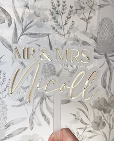 a hand holding up a cake topper with the words mr and mrs nicole on it