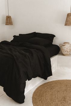 a bed with black sheets and pillows in a room next to two hanging baskets on the wall