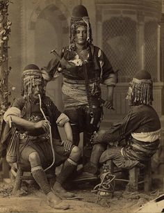 an old black and white photo of three men in native garb sitting on a bench