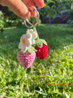 someone is holding two crocheted strawberries in the grass with flowers on them