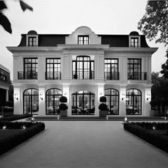 a large white house with lots of windows and plants in the front yard at night