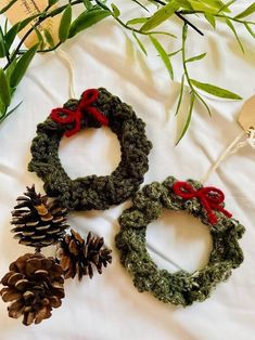 two crocheted wreaths with red bows and pine cones on a white sheet