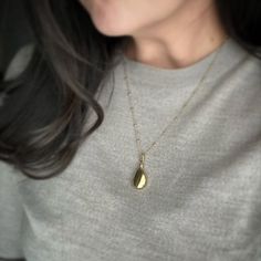 a woman wearing a necklace with a gold tear shaped pendant on it's neck