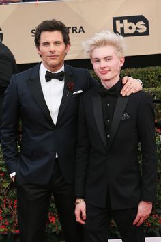 two young men in tuxedos standing on a red carpet at an awards event