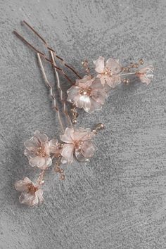 two hair pins with flowers on them sitting next to each other in front of a gray background