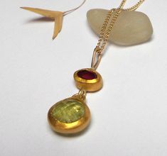 Garnet and Peridot pendant - Beautiful Garnet and Peridot stones inlaid in 24k gold. The Garnet stone size is 4/6mm. The Peridot stone size is 9mm. The Garnet and Peridot pendant length 23mm. The Garnet and Peridot pendant on oxidized sterling silver chain 50cm - 350$. The Garnet and Peridot pendant on 14k solid gold Chain in length 45cm - 530$. Please let me know how do you want the Garnet pendant. Free Shipping The pendant will be packed in a Beautiful gift box. Your necklace will be shipped t Gold Fusion Style Necklaces With Stones, Gold Peridot Gemstone Jewelry, Gold Peridot Jewelry With Gemstone, Gold Necklaces With Oval Pendant And Stones, Gold Peridot Round Pendant Necklace, Gold Necklace With Round Peridot Pendant, Gold Peridot Necklace For Formal Occasions, Gold Fusion Pendant Necklace, Yellow Gold Pendant Necklace With Stones