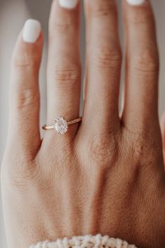 a woman's hand wearing a gold ring with a white diamond on the middle