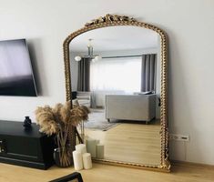 a large mirror sitting on top of a wooden floor next to a vase filled with flowers