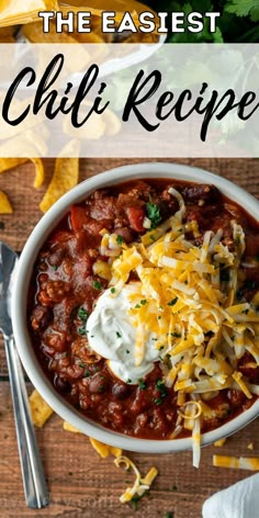 a bowl of chili with cheese, sour cream and tortilla chips on the side