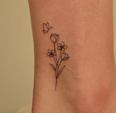 a small flower tattoo on the side of a woman's ankle, with butterflies flying around