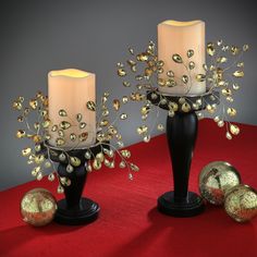 two candles are sitting next to each other on a red tablecloth with gold balls