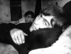 black and white photograph of two men laying in bed with one man looking at the camera