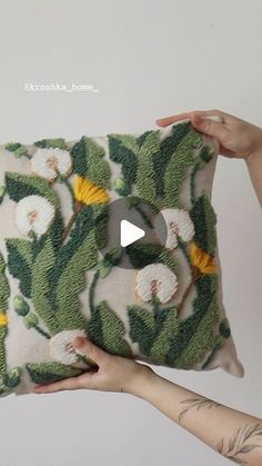 two hands holding up a green and white floral pillow with yellow flowers on it's sides