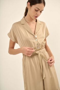 Matte-finish satin jumpsuit. Notch lapel collar. V neckline. Short kimono sleeves. Button front closure with pearly shell buttons. Drawstring elastic waist. Hip pockets. Side cargo pockets with strap closure. Wide leg. Relaxed fit. 100% Polyester. Imported. Designed in LA. Model wears size S. Cargo Jumpsuit, Satin Jumpsuit, Kimono Sleeves, Short Kimono, Matte Satin, Shell Buttons, Kimono Sleeve, Iron Decor, Lapel Collar