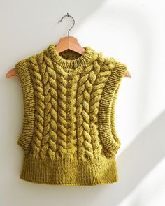 a yellow sweater hanging on a wooden hanger with a white wall in the background