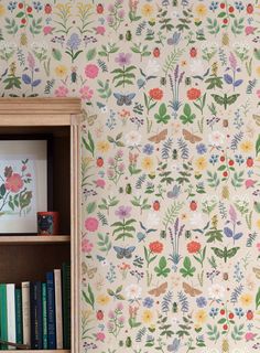 a bookshelf filled with lots of books next to a wall covered in flowers