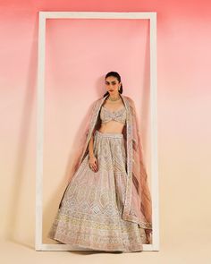 a woman standing in front of a pink wall wearing a white and beige lehenga