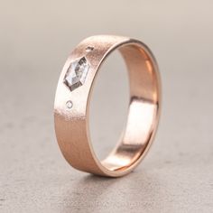 a rose gold wedding ring with a diamond set in the center, on a gray surface