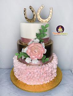 a three tiered cake with flowers and horseshoes on top is decorated in pink, white, and gold