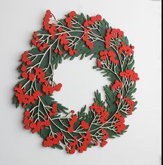 a paper wreath with red berries and green leaves on white background, hanging from the wall