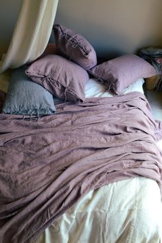 an unmade bed with purple sheets and pillows