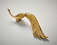 a gold brooch with a bird on it's back and long tail, sitting on a white surface