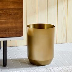 a gold vase sitting on top of a white floor next to a wooden table and chair