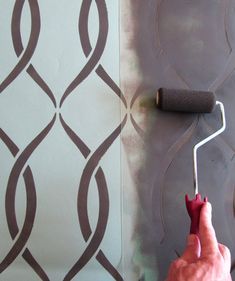 a person using a paint roller to paint a wall with decorative designs on it,