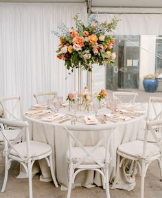 a table set up with white chairs and flowers in vases on the centerpiece