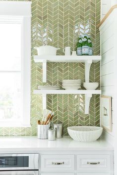 a kitchen with white cabinets and green tile on the wall, along with an open window