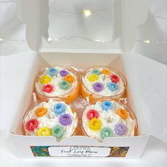 four cupcakes in a white box with colorful frosting and flowers on them