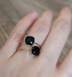 a woman's hand holding two rings with black stones on each ring and gold band