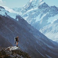 a man standing on top of a mountain next to a large snow covered mountain range