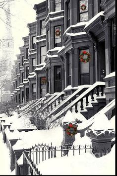 a row of houses covered in snow with christmas wreaths on the windows