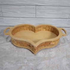 a heart shaped wooden tray with handles on a counter top next to a white wall