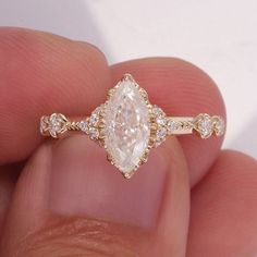 a close up of a person's hand holding a ring with an oval shaped diamond