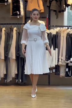 a woman in a white dress walking through a clothing store