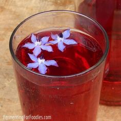 two glasses filled with red liquid and blue flowers