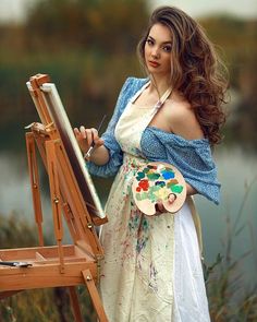 a woman is holding a paintbrush and painting on an easel