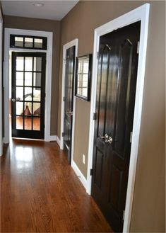 an empty hallway with two black doors and wood flooring on either side of the door