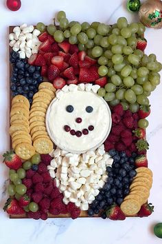 a platter with grapes, strawberries, crackers and other fruit arranged in the shape of a face