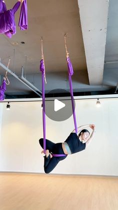 a woman is doing aerial acrobatics in an empty room with purple tassels hanging from the ceiling