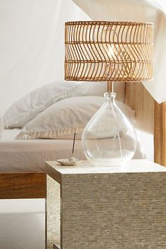 a lamp that is sitting on top of a table next to a bed with white sheets