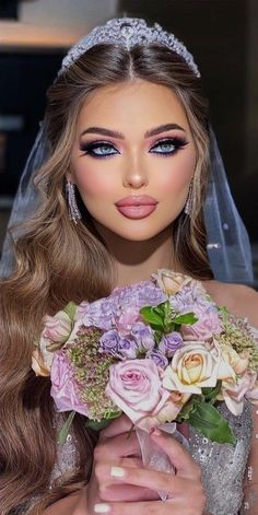 a woman in a bridal gown holding a bouquet of flowers and wearing a tiara