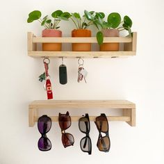 three wooden shelves holding sunglasses, keys and plants on top of each shelf are hanging from the wall