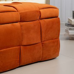 an orange footstool sitting on top of a white floor next to a window