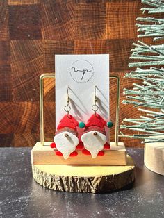 two red and white santa hats are hanging from earrings on a wooden stand next to a christmas tree