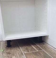 a white shelf sitting on top of a wooden floor next to a wall with holes in it